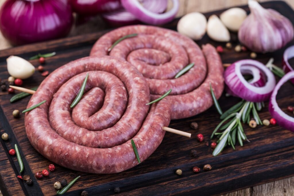 Zwei Bratwurstschnecken auf Holzbrett mit Zwiebeln und Rosmarin als Dekoration